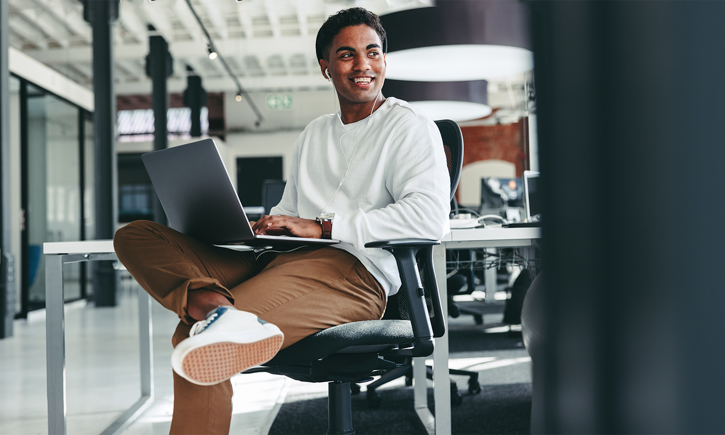 Smiling developer sitting cross legged in a chair with a laptop on his lap